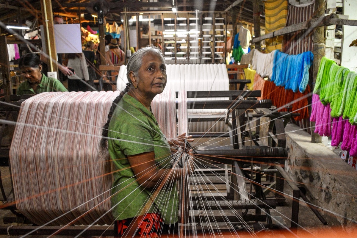 A weaver working at a traditional handloom at Sooriya Weaving Mills in Galle, surrounded by colourful dyed yarn